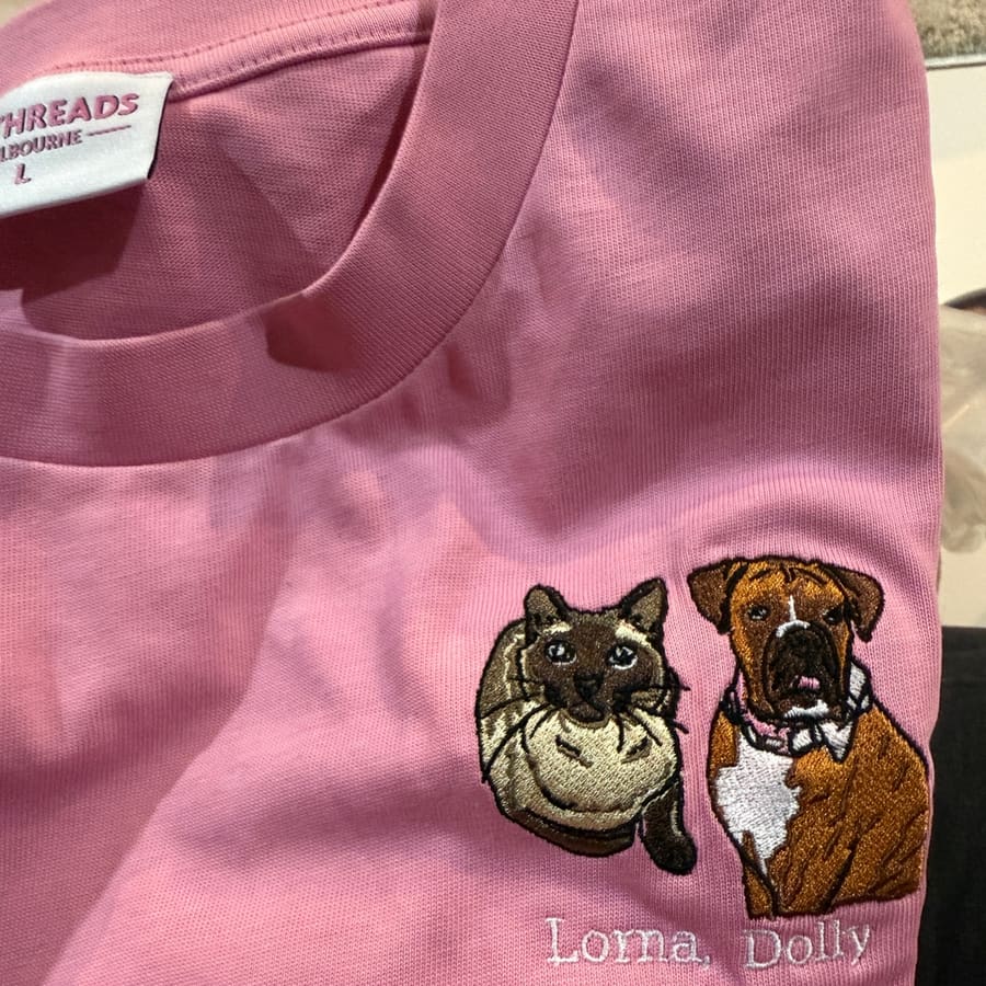 Close-up of an embroidered cat and dog pet portrait on a folded pink tee