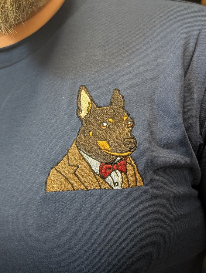 Dense satin-stitch dog portrait in a tuxedo embroidered on a navy tee, close up